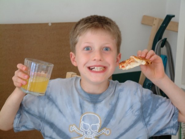 Brand designer as a child, smiling and holding a slice of pizza and an orange drink.