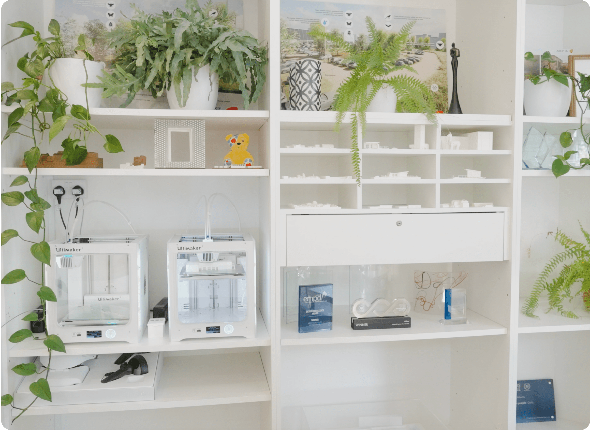 Architectural models and 3D printers displayed in a bright architecture studio.