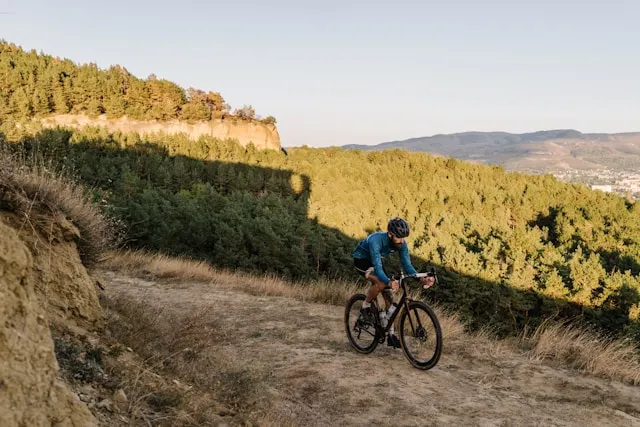 Cyclist descending a hillside trail surrounded by trees and open landscape