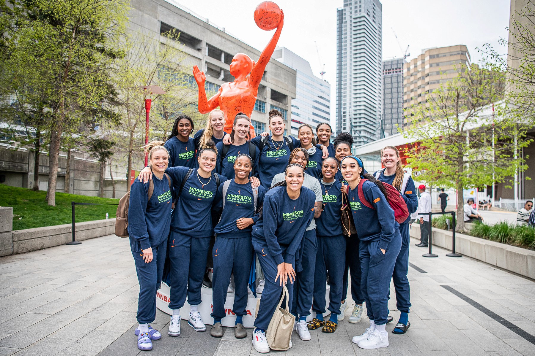 A child in a swimsuit playfully jumps with a water spray in a backyard, surrounded by toys and greenery.