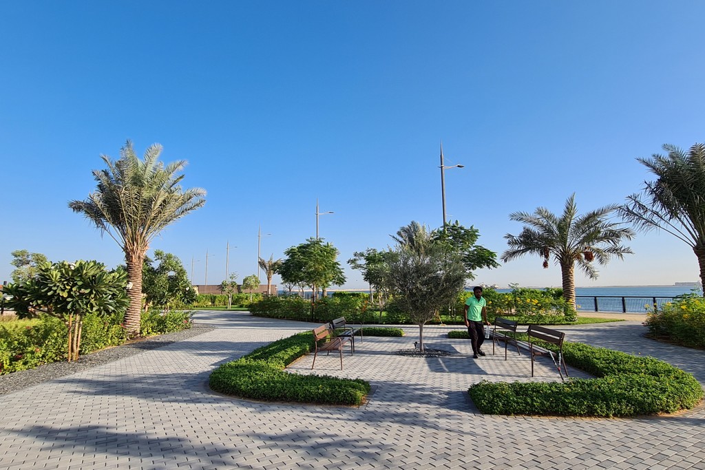 A scenic view of Dubai Maritime City park featuring lush greenery, walking paths, and modern architecture in the background.
