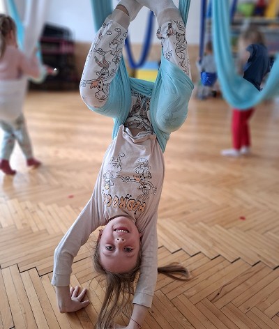 Dítě visící hlavou dolů v modré síti při lekci fly jógy