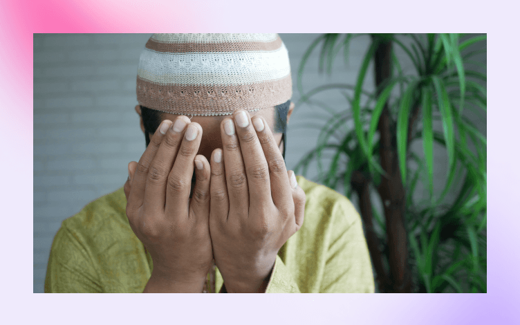 Individual with hands covering face in a gesture of prayer, wearing a knit cap, symbolizing a personal moment of making dua or supplication.