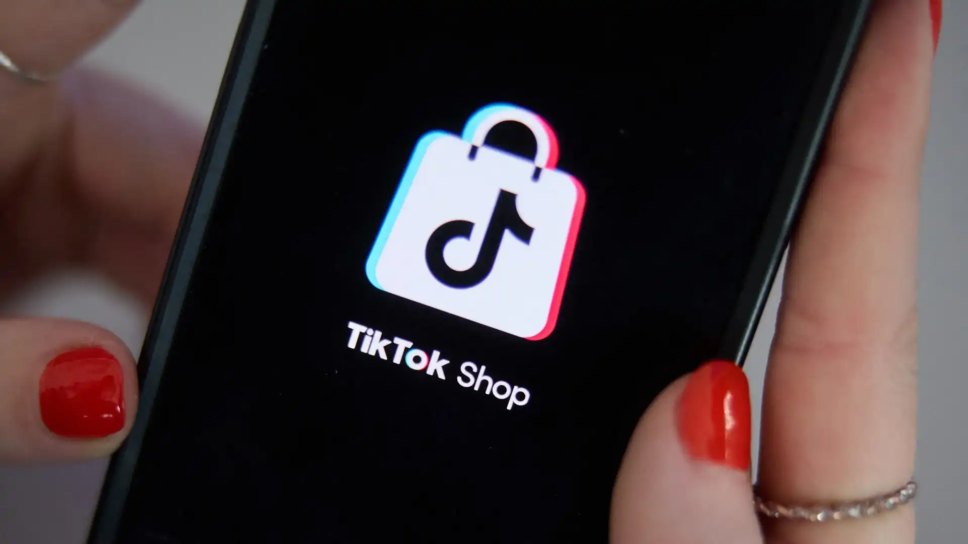 A close-up of a hand holding a smartphone showing the TikTok Shop logo, representing the platform's direct integration of shopping.
