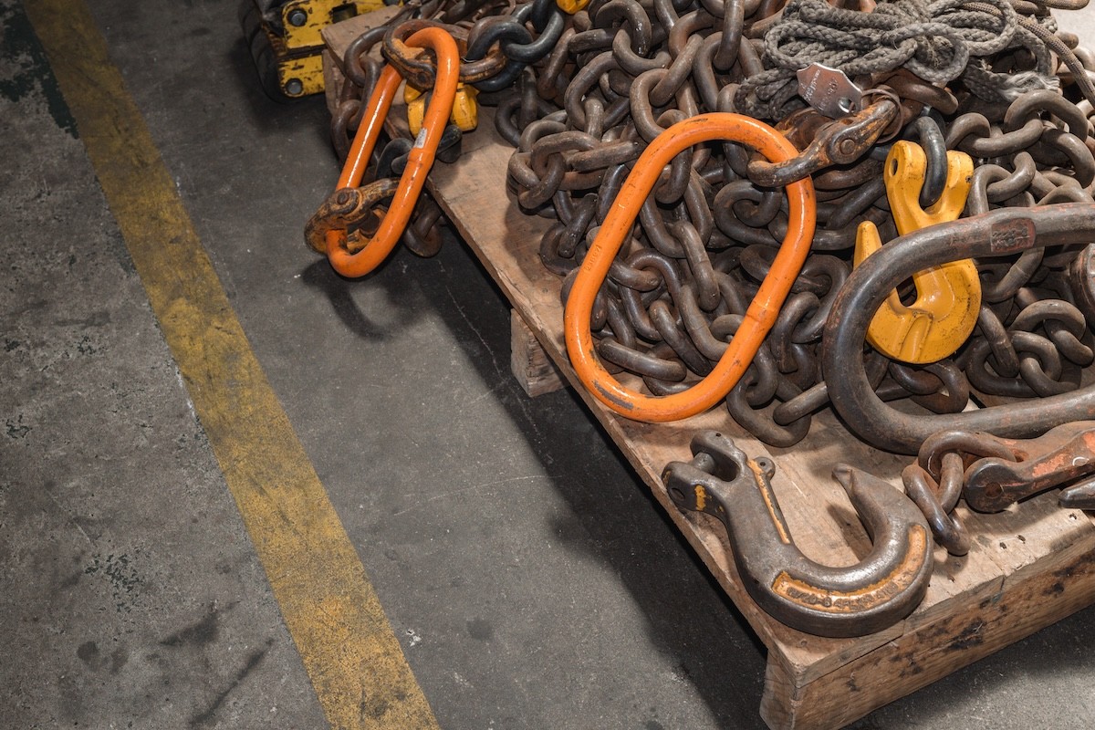 Heavy-duty industrial lifting tackle including orange master links, chains, and hooks on a pallet.