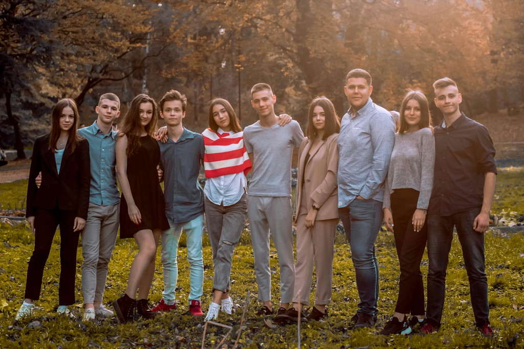 A group of young adults stands together in a park, posing for a photo with smiles and casual attire, capturing a moment of friendship and unity in a natural outdoor setting.