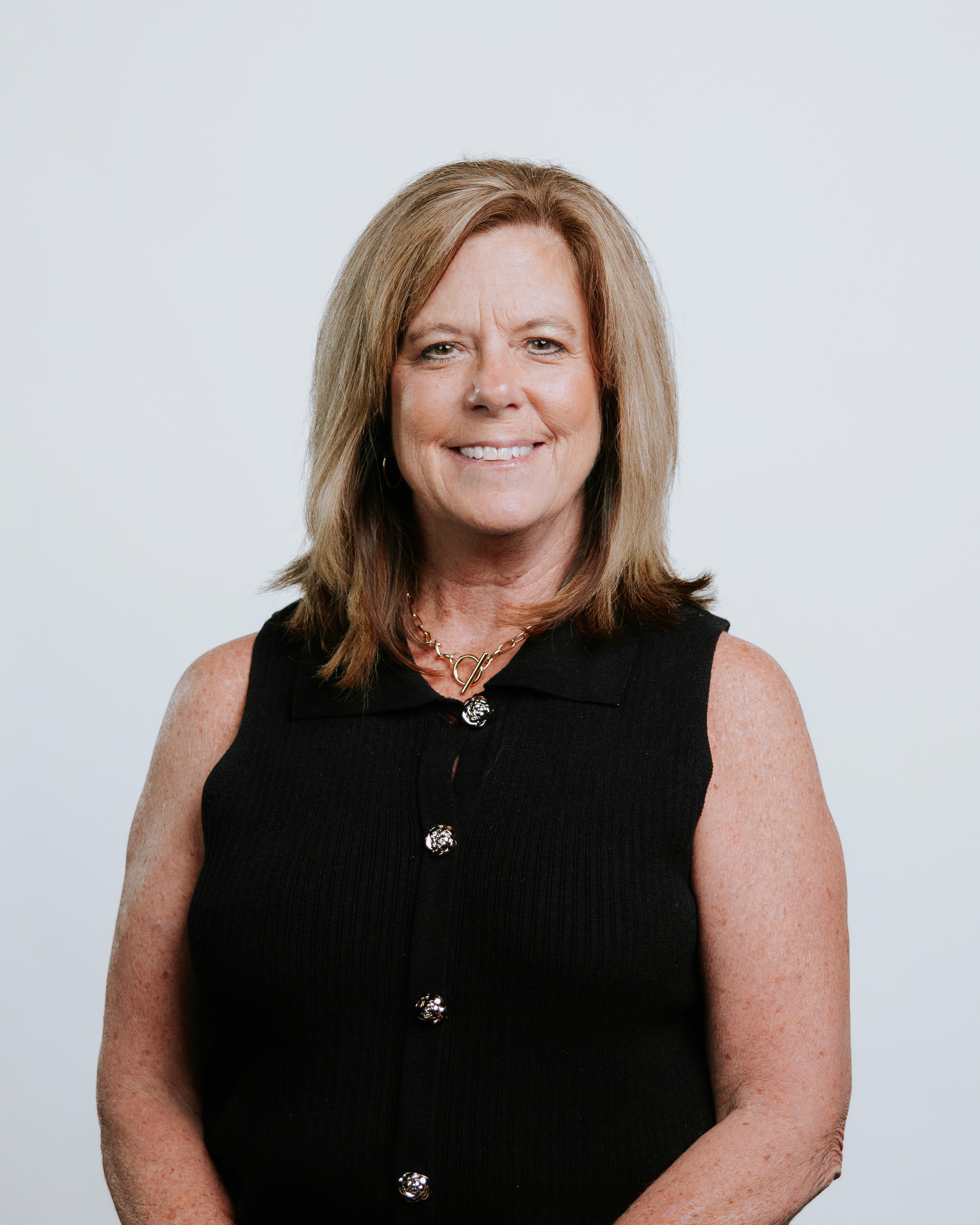 A woman with shoulder-length hair smiles, wearing a green shirt and black leather jacket against a plain background.