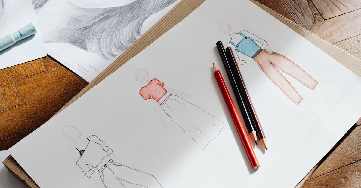 Artistic fashion design sketches on paper accompanied by colored pencils on a wooden surface.
