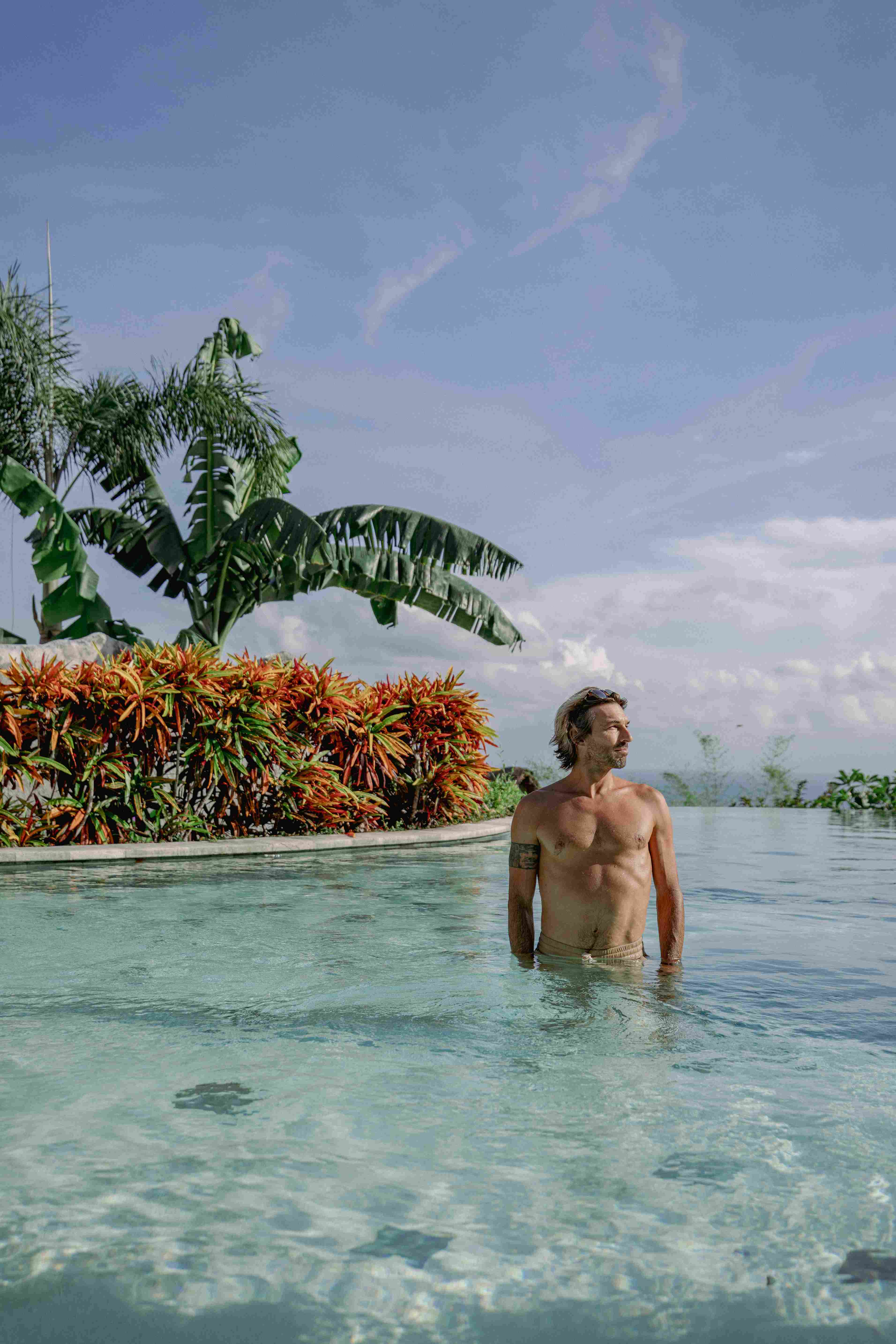 Male student relaxing in the infinity pool overlooking the ocean at Ulu Yoga retreat center.