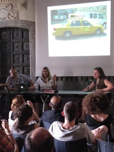 A photo of three persons giving a lecture while behind them is a screen with a projected American Yellow Cab and a white van.