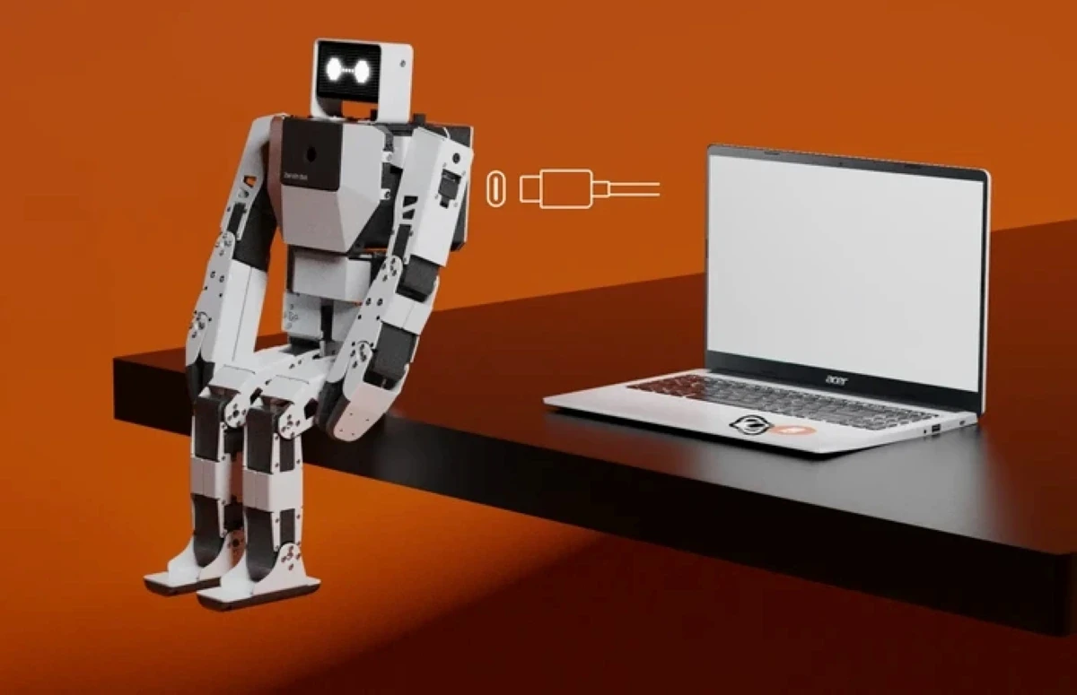 A robot with a rectangular, white and black body sits on the edge of a sleek, black table beside an open laptop, set against a solid orange backdrop, while a graphic indicating a USB connection hovers in the air.