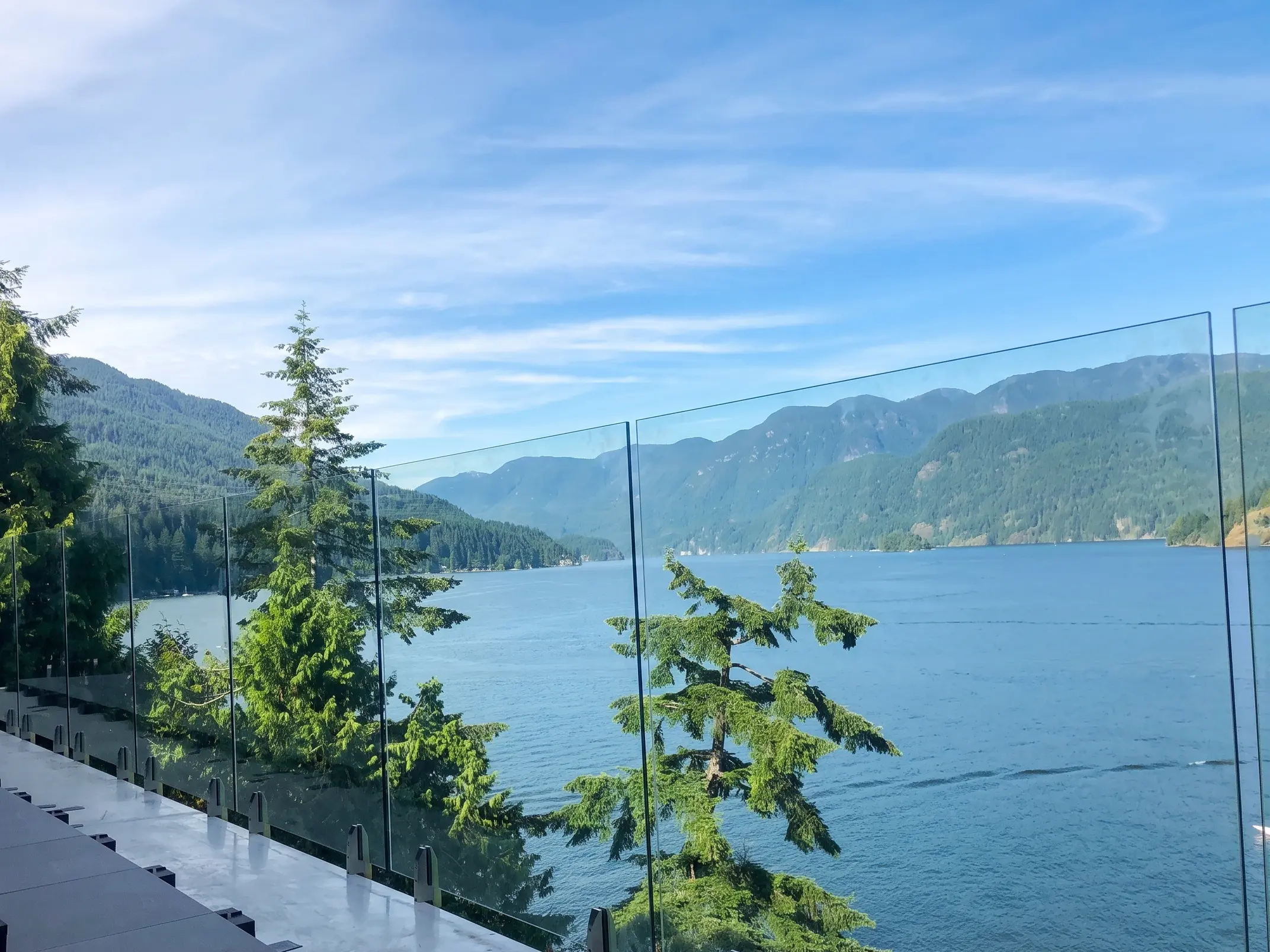 Frameless glass railings on a Parksville BC oceanview deck overlooking the Strait of Georgia and forested mountains across the water.