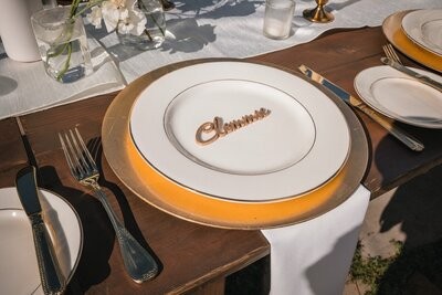 A place setting with a gold charger and a wooden Clemmie name marker on the white plate.