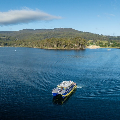 一艘蓝黄相间的船在平静的湖面上航行，岸边树木成荫，远处是层叠的山丘，天空湛蓝。