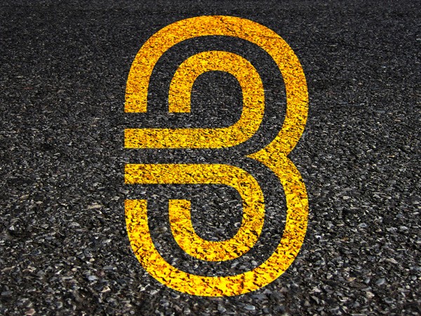 A stylized road design featuring a large white number "3" representing a three-way intersection, with symbols for a bicycle and a car, along with the text "NYC GOES THREE WAYS" and the website "3WAYSTREET.ORG" displayed below, all set against a dark asphalt background.