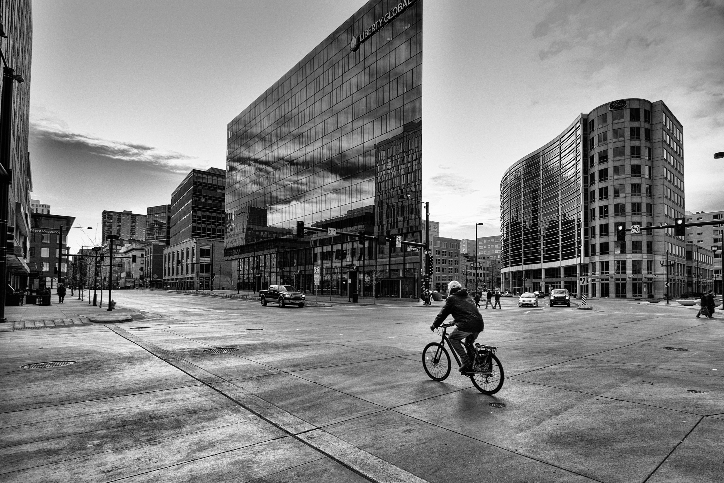 Person on a bicycle riding through an empty, modern city plaza surrounded by glass buildings