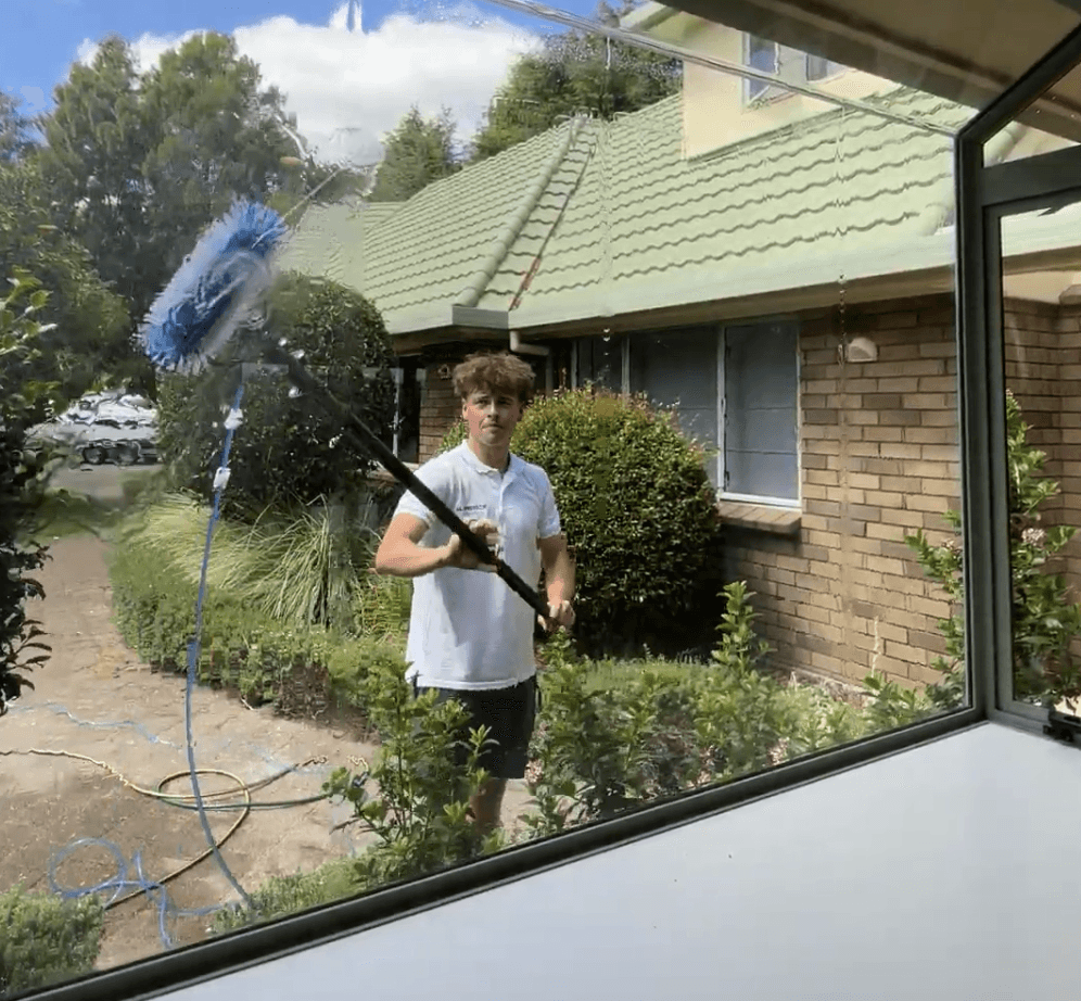 Josiah cleaning upper-storey windows on a Waikato property using a purified water system