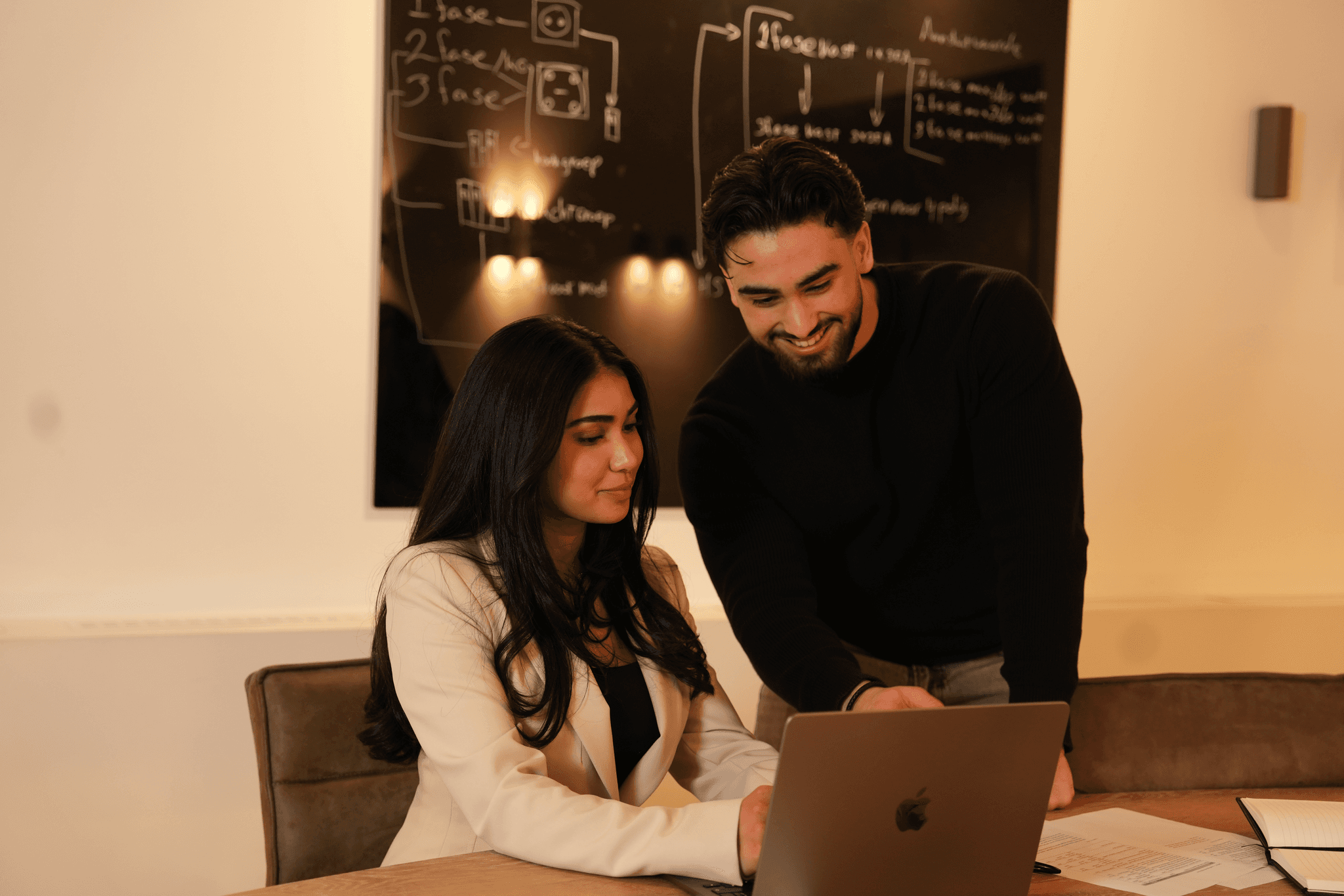 Black and white photo of two people looking at a computer screen with papers on wall