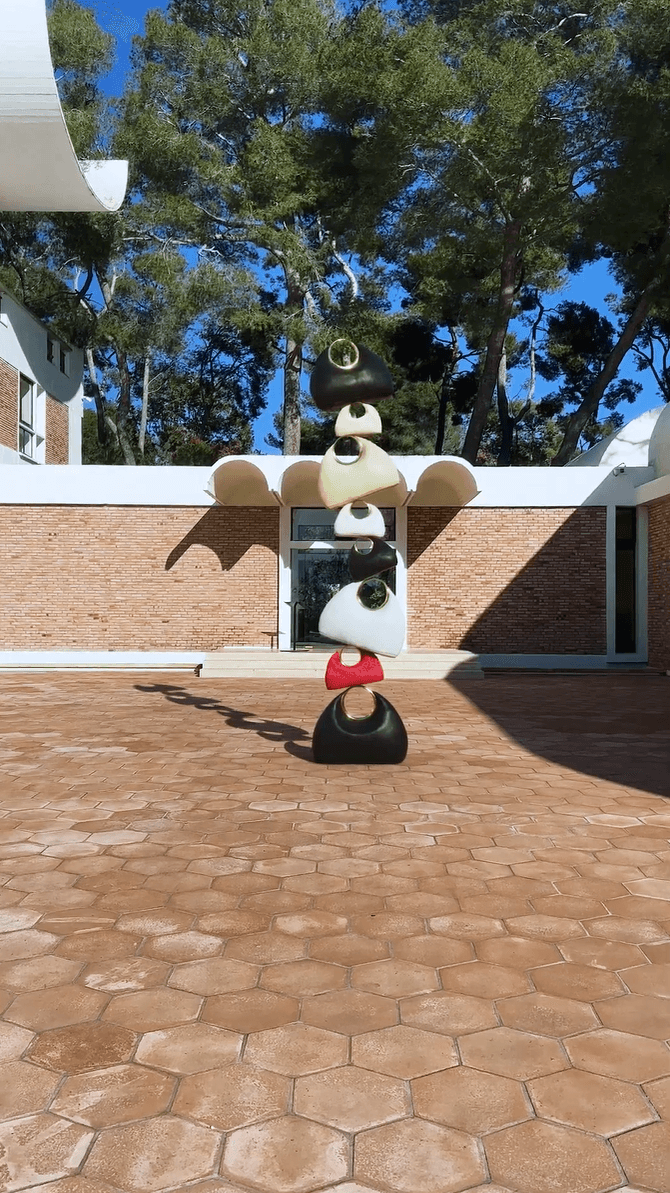 A unique stacking sculpture of various colored Jacquemus handbags outside a brick building