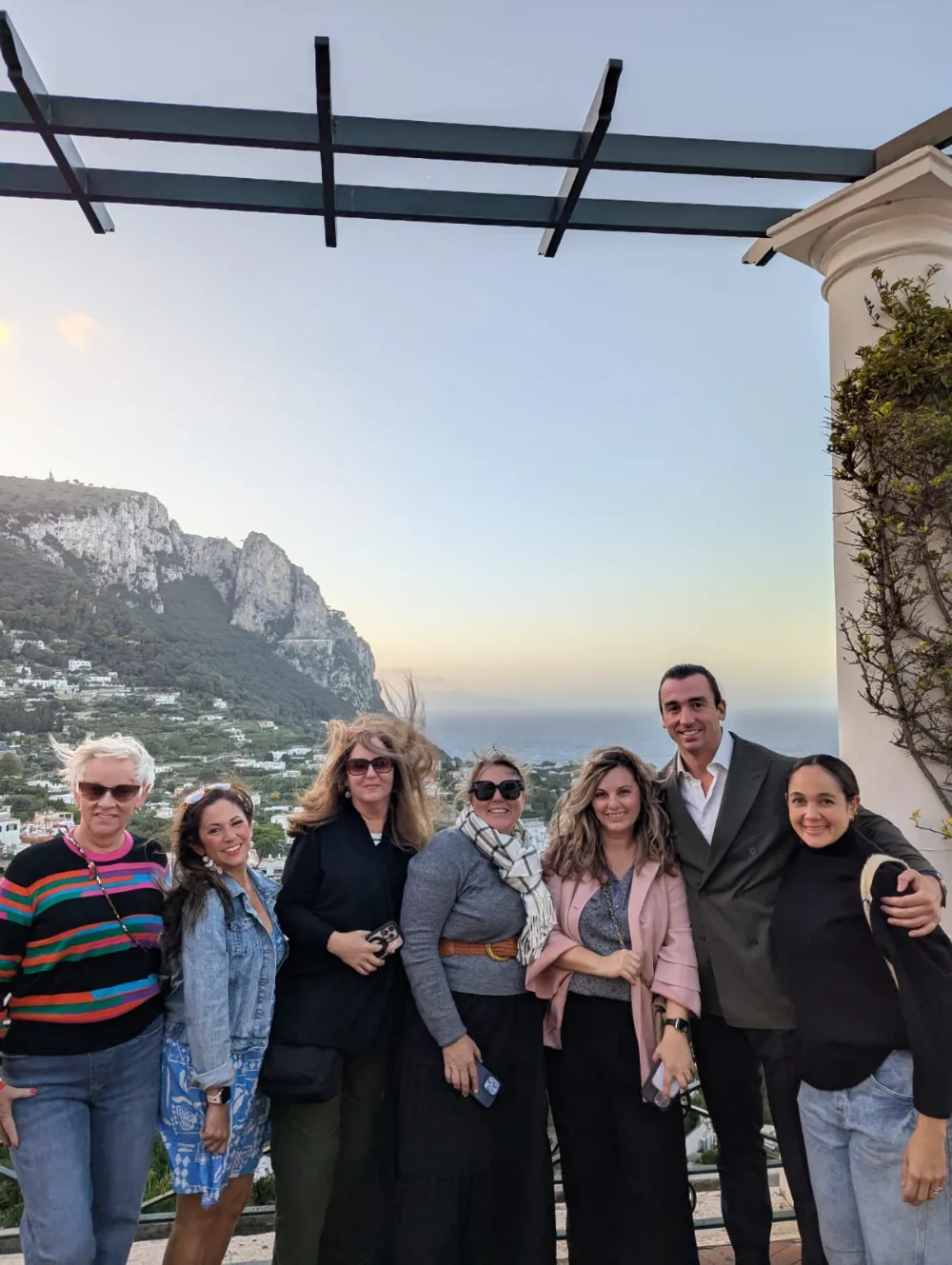 A group of travellers on a terrace at sunset, with Capri's hills behind them.