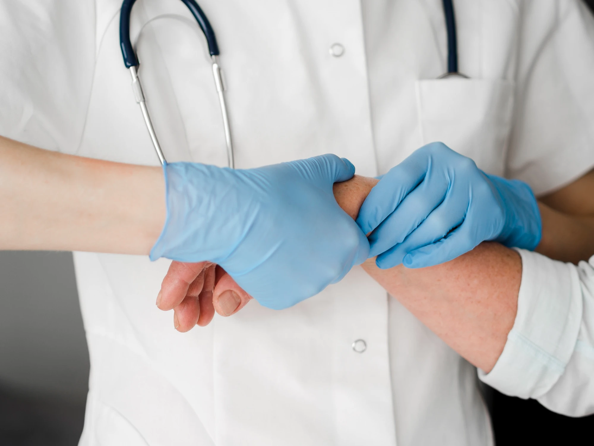 A doctor in a white coat with a stethoscope checks a patient's pulse. The doctor wears blue gloves, conveying a sense of care and professionalism.