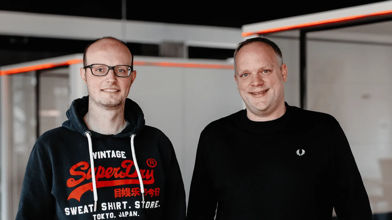 Zwei Männer stehen gemeinsam in einem Büro und lächeln in die Kamera steht für das Team und die Gründerkultur von mercury.ai