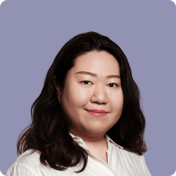 A smiling black haired woman in a white shirt in front of a purple background