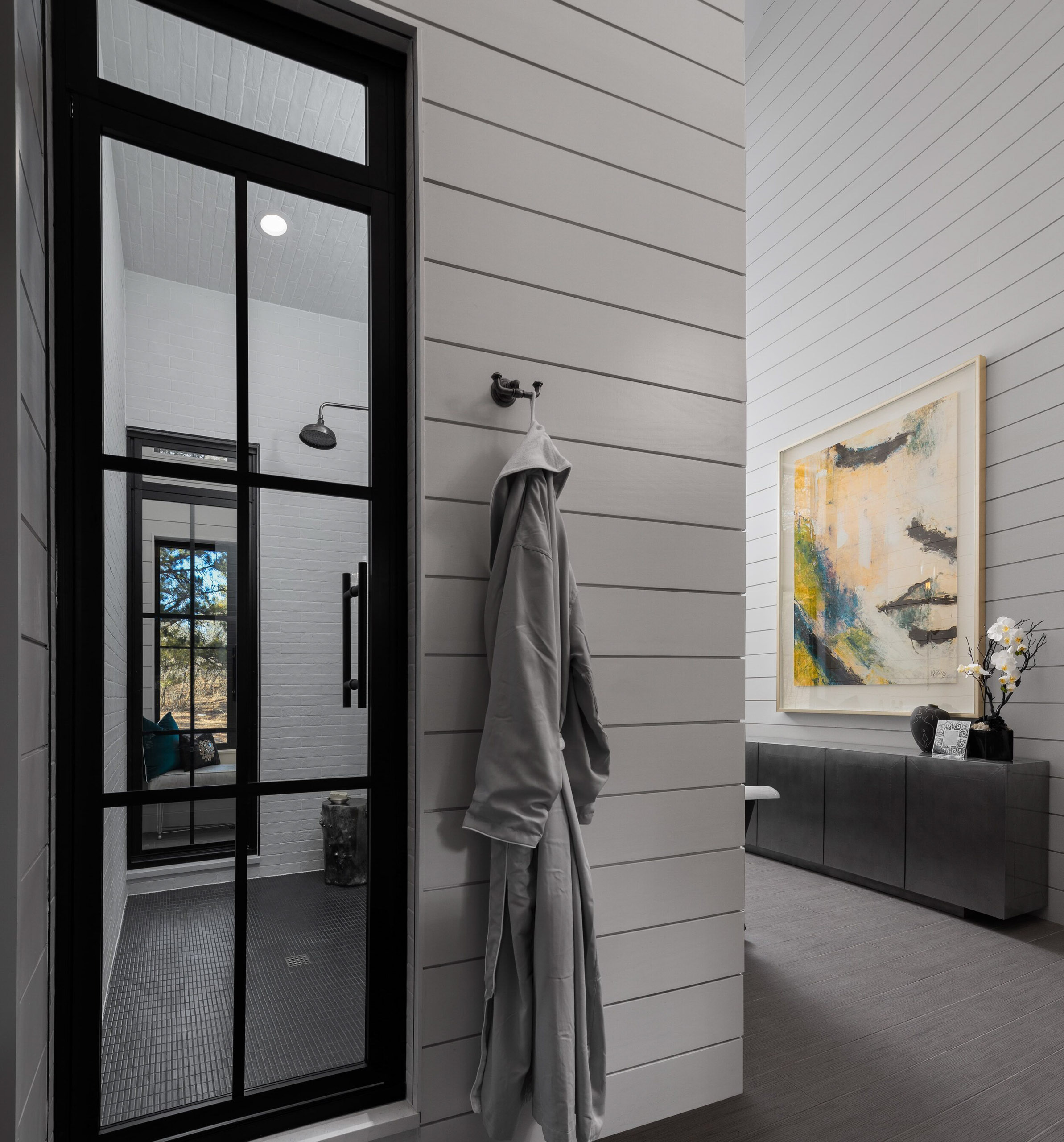 Modern bathroom with shower, artwork, and robe.