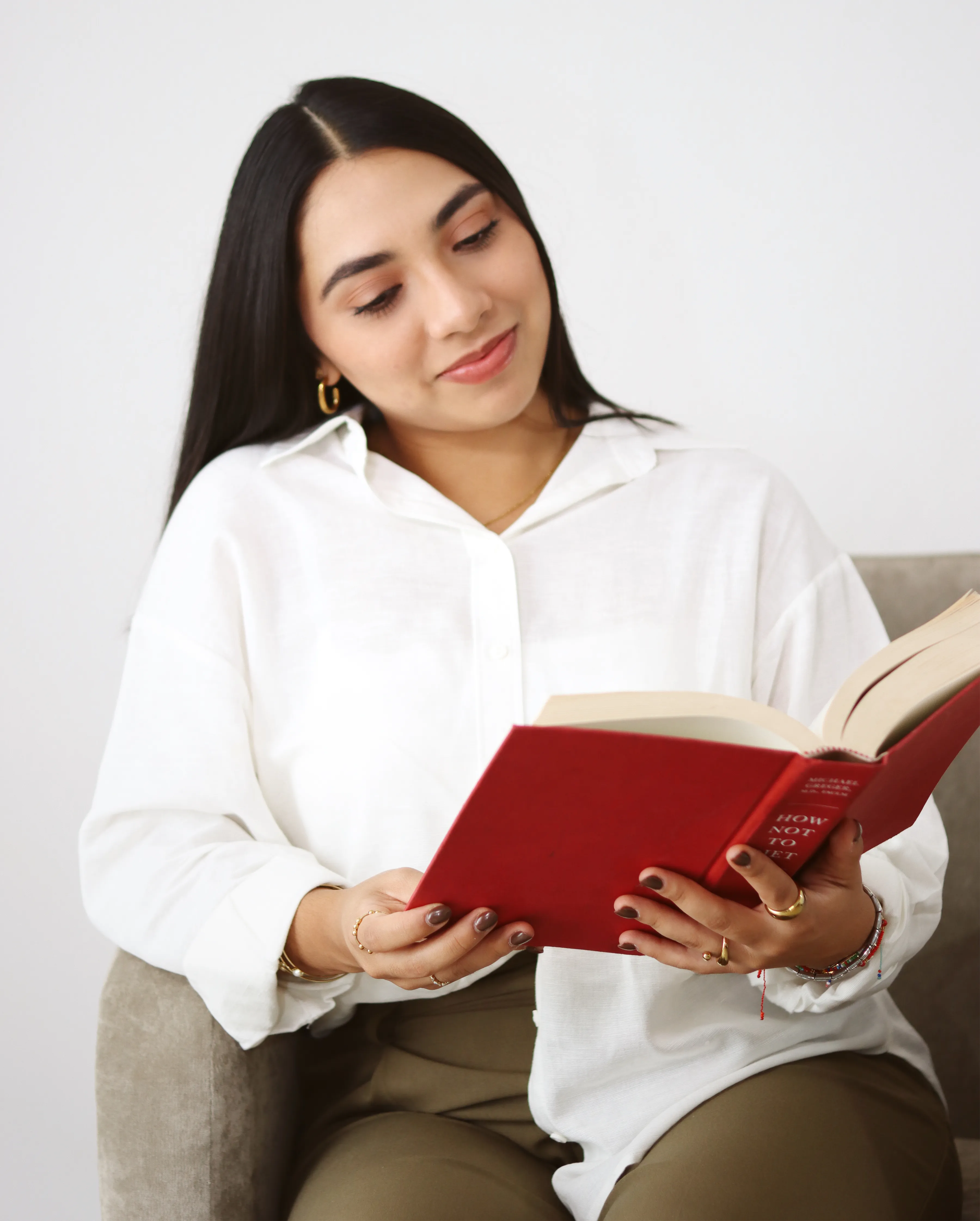 Nutrióloga leyendo libro de tapa roja sentada en sillón beige.