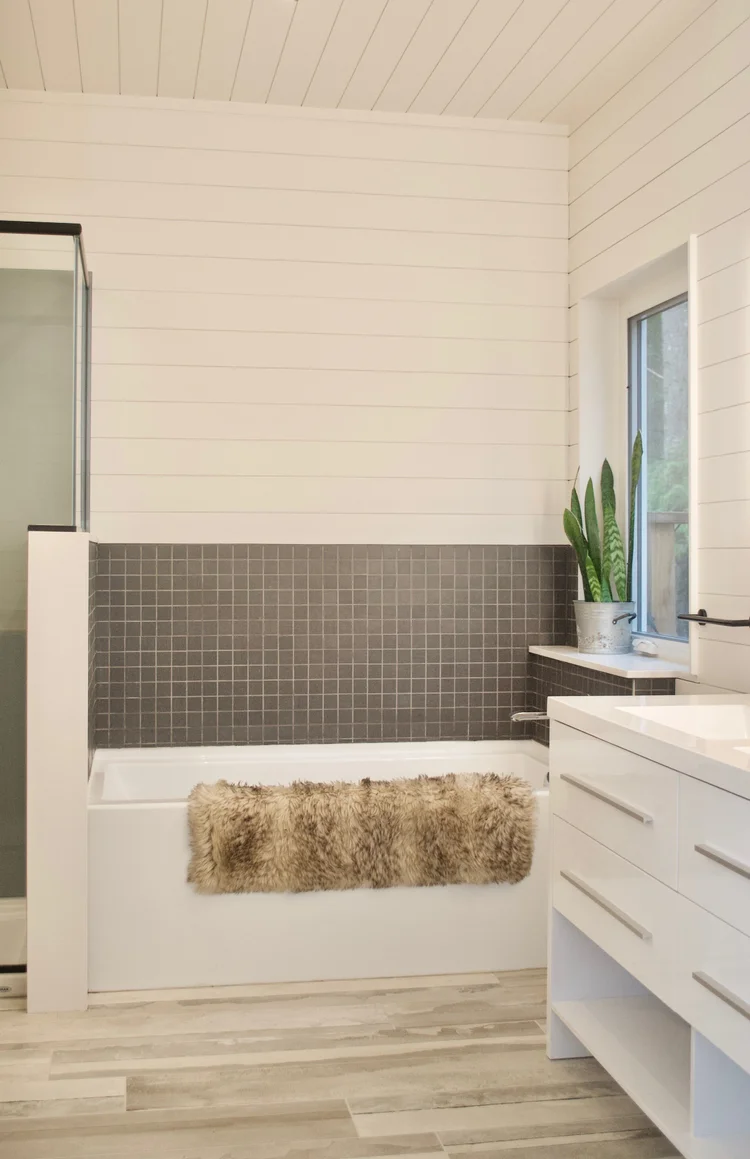 Modern two-story home with large glass windows, warmly lit interiors, and a balcony. Surrounded by trees and a manicured lawn at dusk. Cozy ambiance.