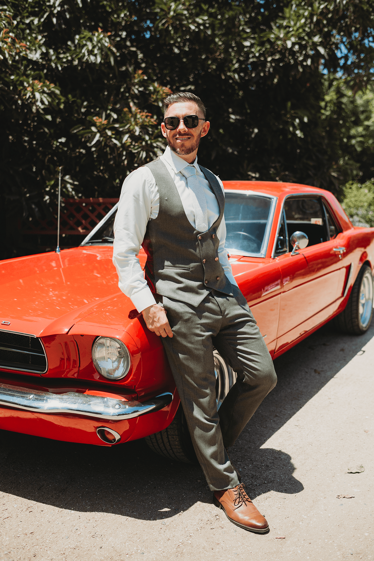 Groom leaning on red 1948 Mustang at Gerry Ranch wedding