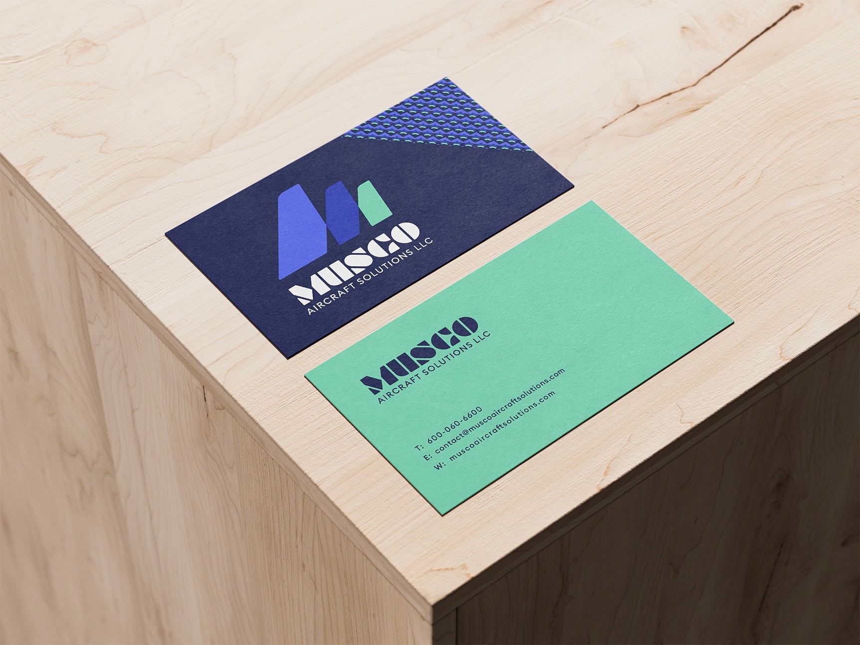 Graphic design mockup of business cards on a wooden table for Musco Aircraft Solutions — modern, geometric wordmark logo with a clean brandmark with a clean sans serif typography, designed by Will Lefkovich.