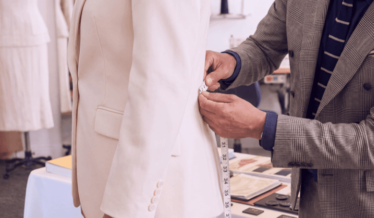 Bespoke tailor measuring the fit of an ivory women’s wedding suit during a custom suit fitting.