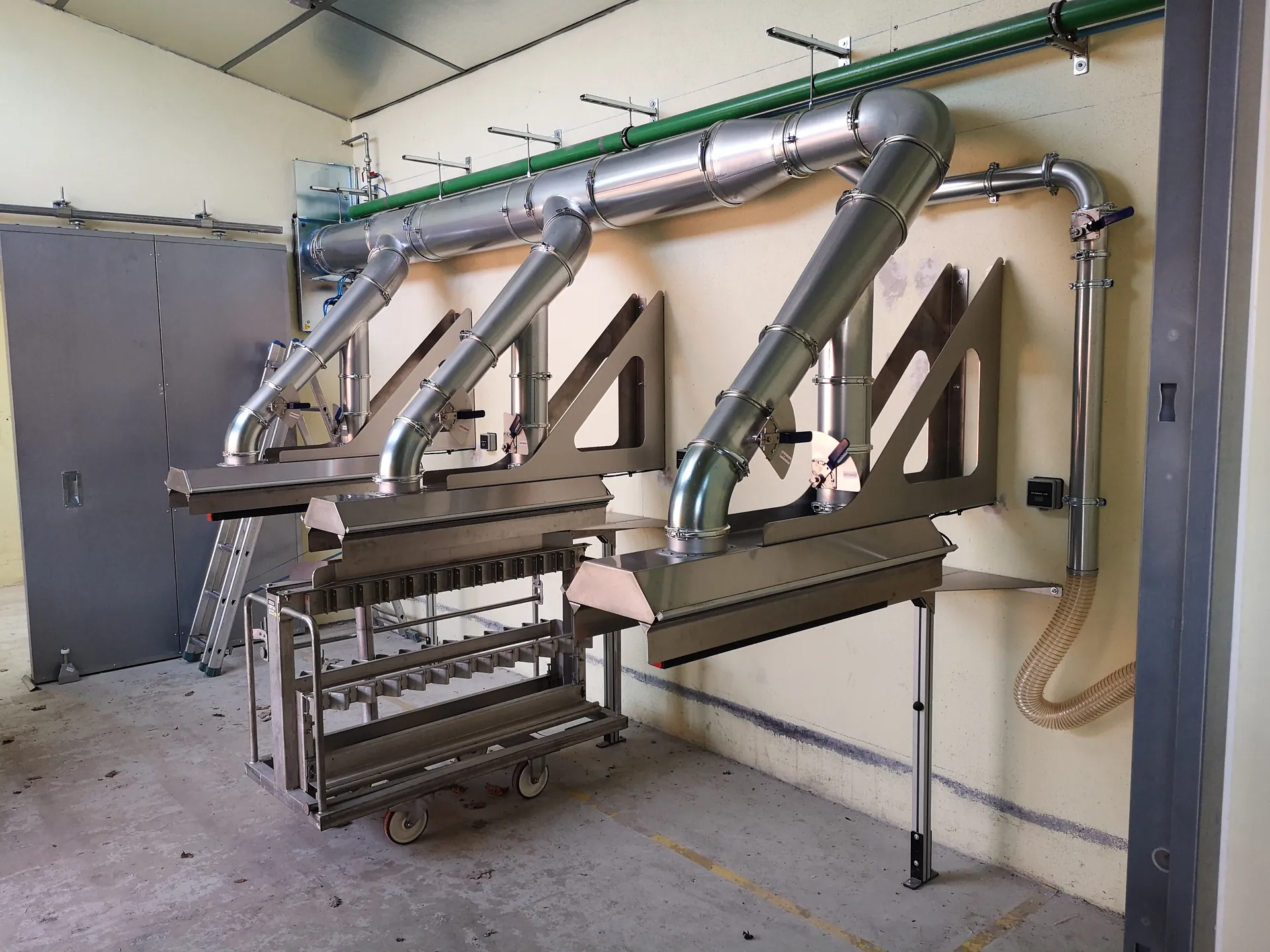 Réseau de gaines métalliques et dispositifs de captation installés au-dessus de postes de travail dans un atelier industriel.