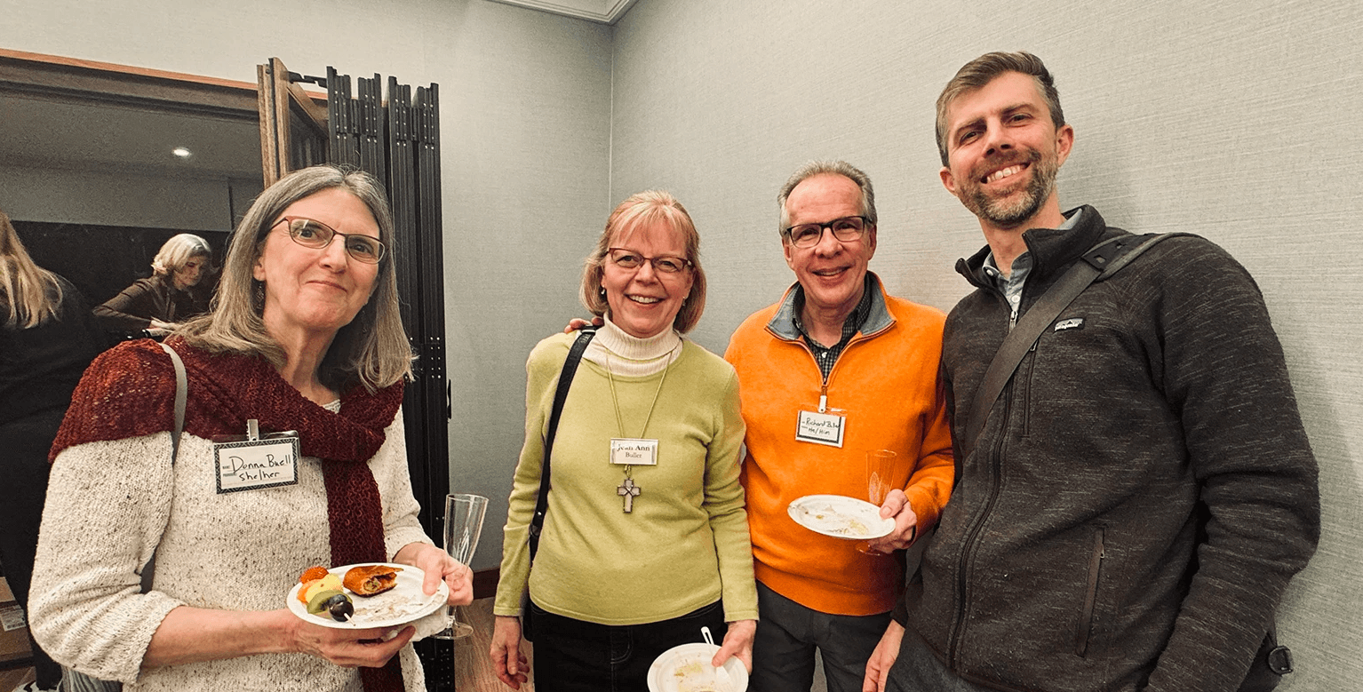 Group of four Grace Trinity Church members standing together, enjoying food and drinks during a casual event.