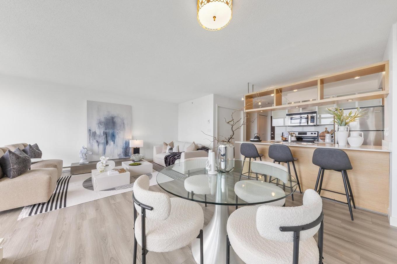 A modern dining area featuring a glass table, white chairs, and an open kitchen in a bright, airy space.