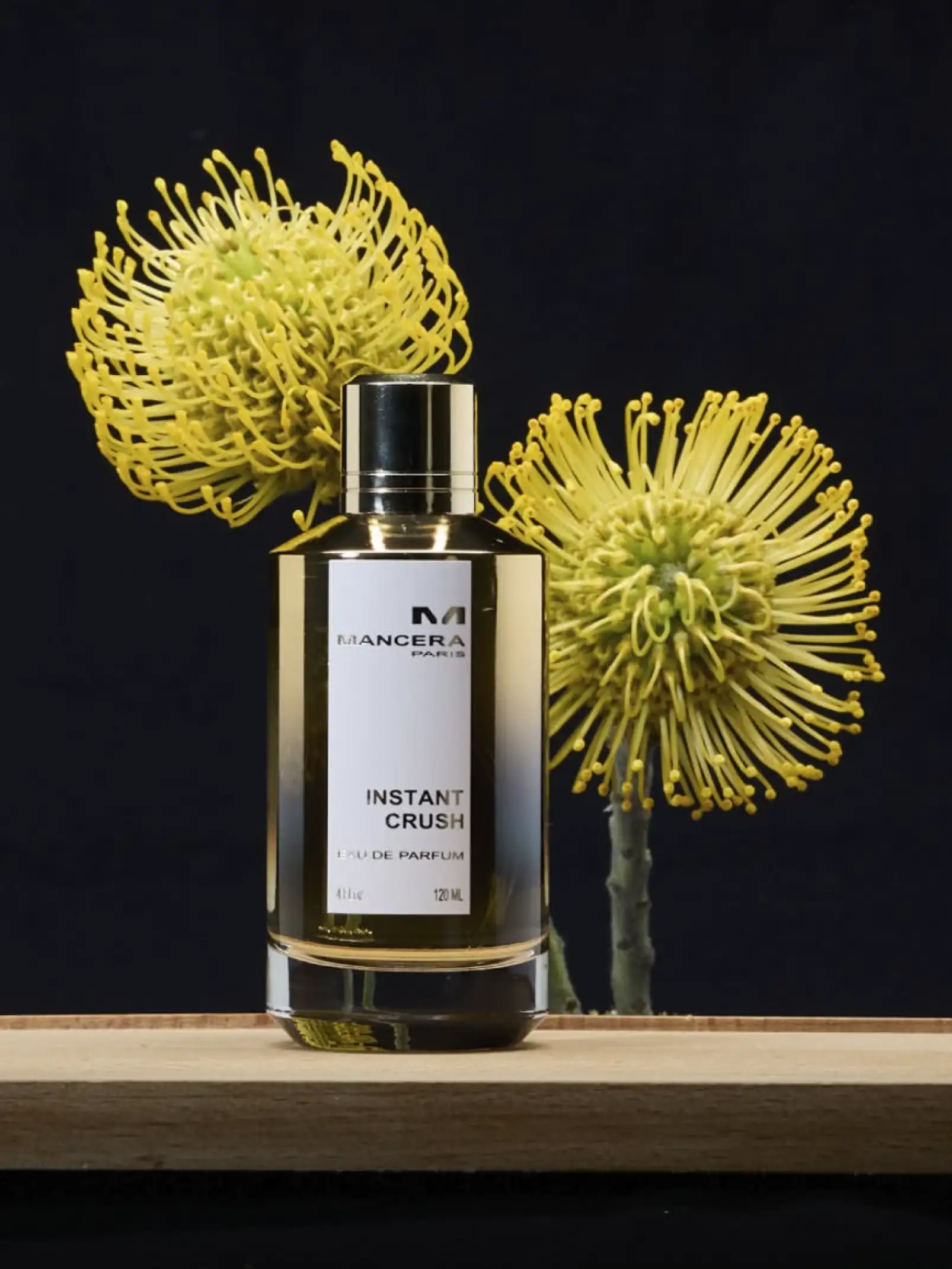 Perfume Instant Crush con flores amarillas detrás para campaña de perfumería premium con enfoque floral moderno.