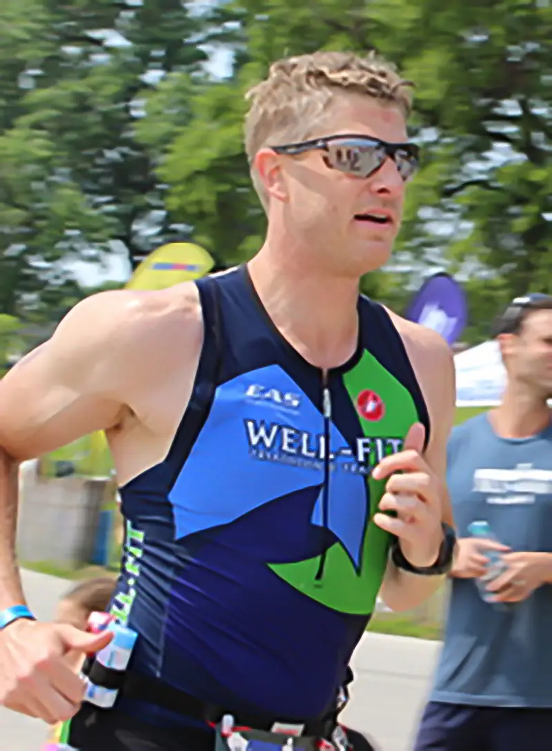 Male Well-Fit triathlete in focused concentration during the run leg of a triathlon race, wearing a Well-Fit Triathlon Training kit