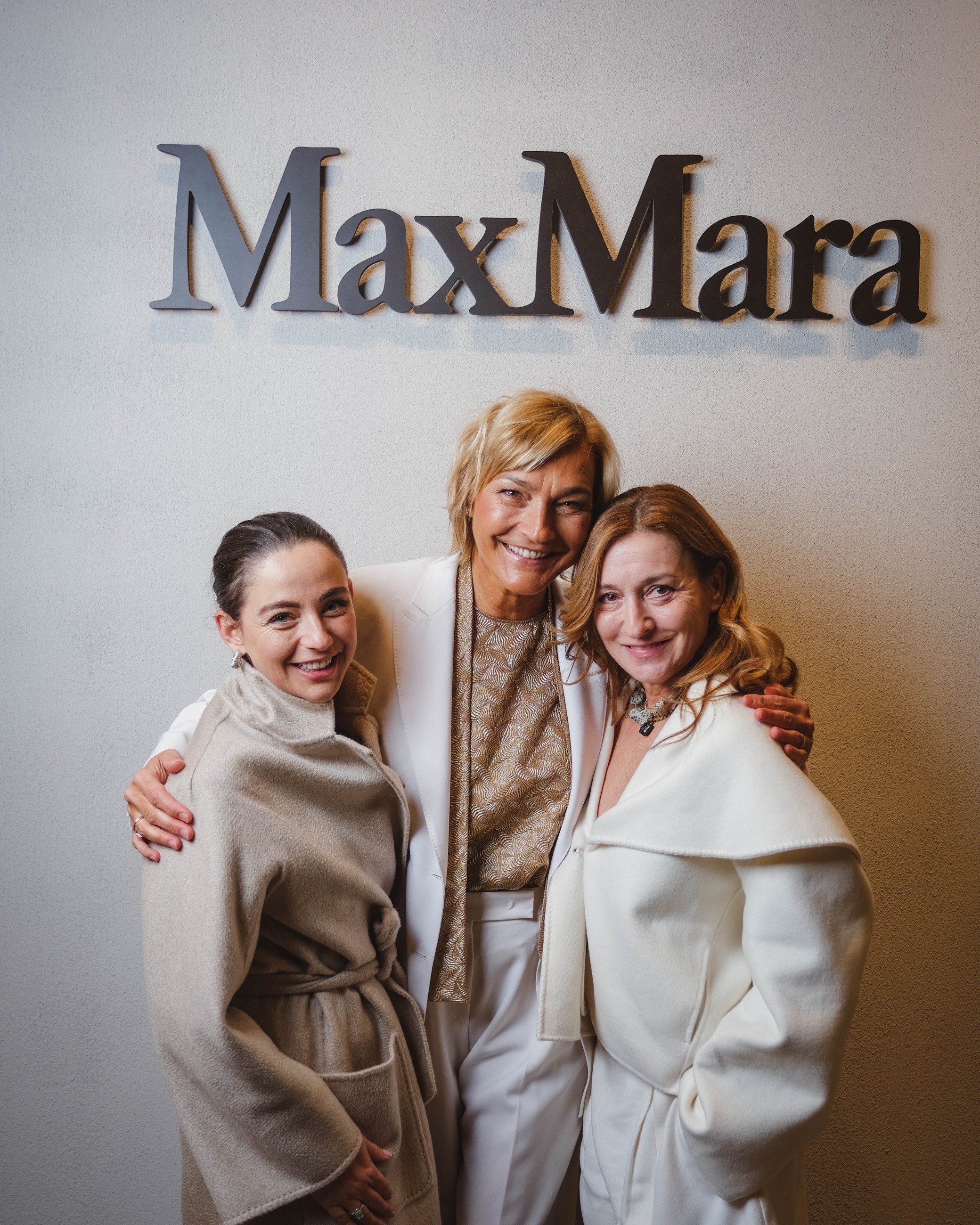 Three guests smiling together in pale coats at the Max Mara event