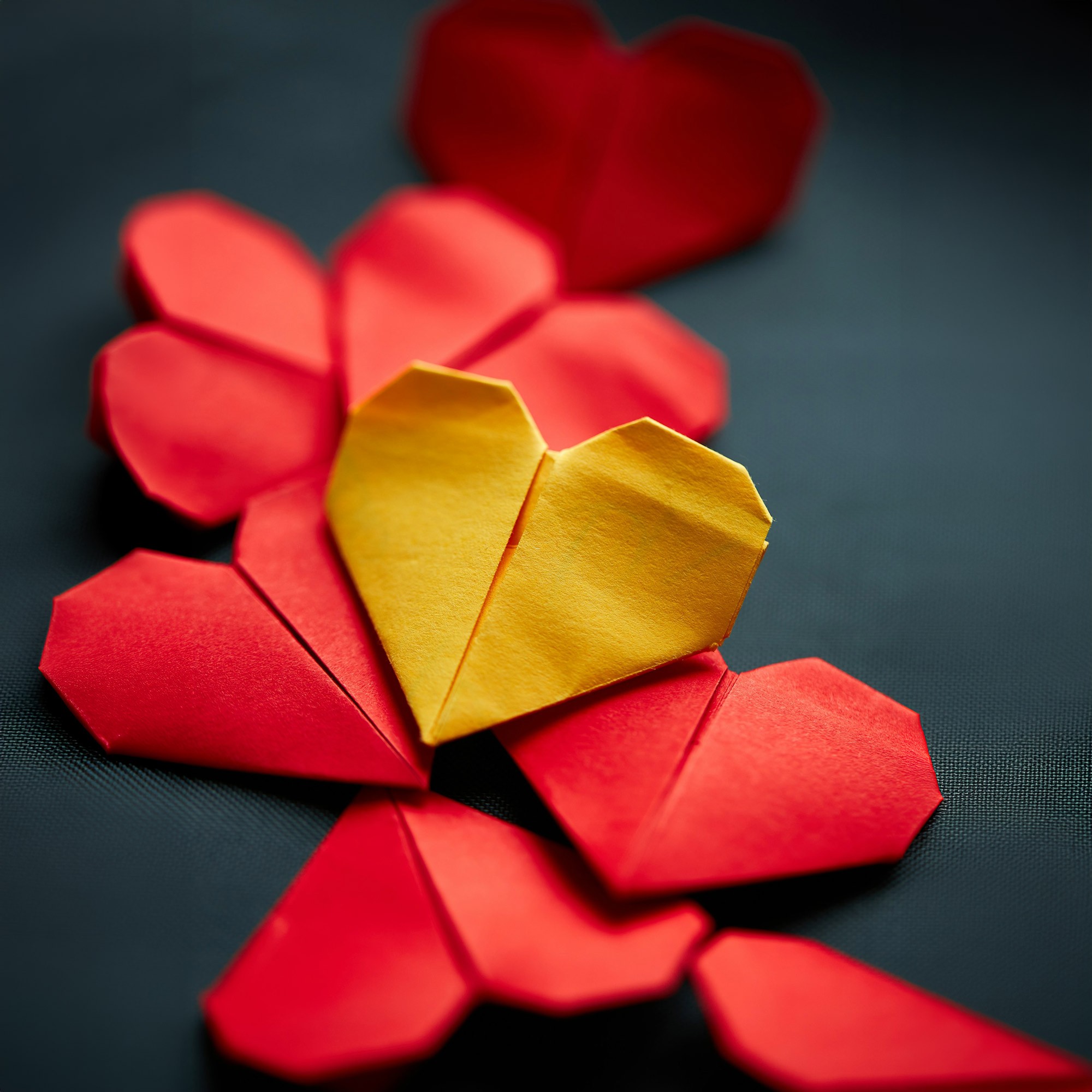 Mehrere rote und ein goldenes Origami-Herz auf dunklem Untergrund, das goldene Herz liegt in der Mitte
