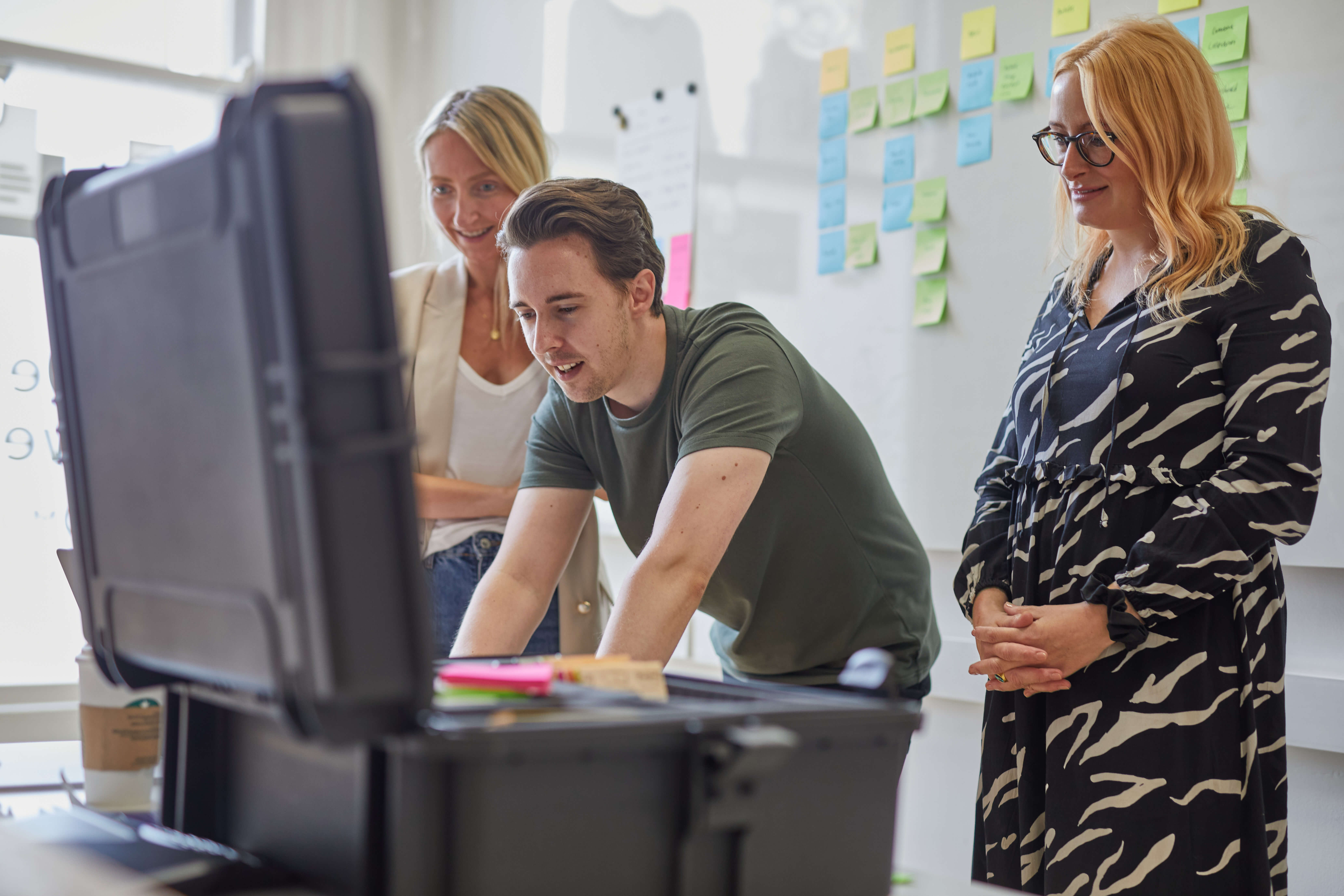 Three members of staff in front of a whiteboad in the Komodo studio sort brightly coloured post-it notes