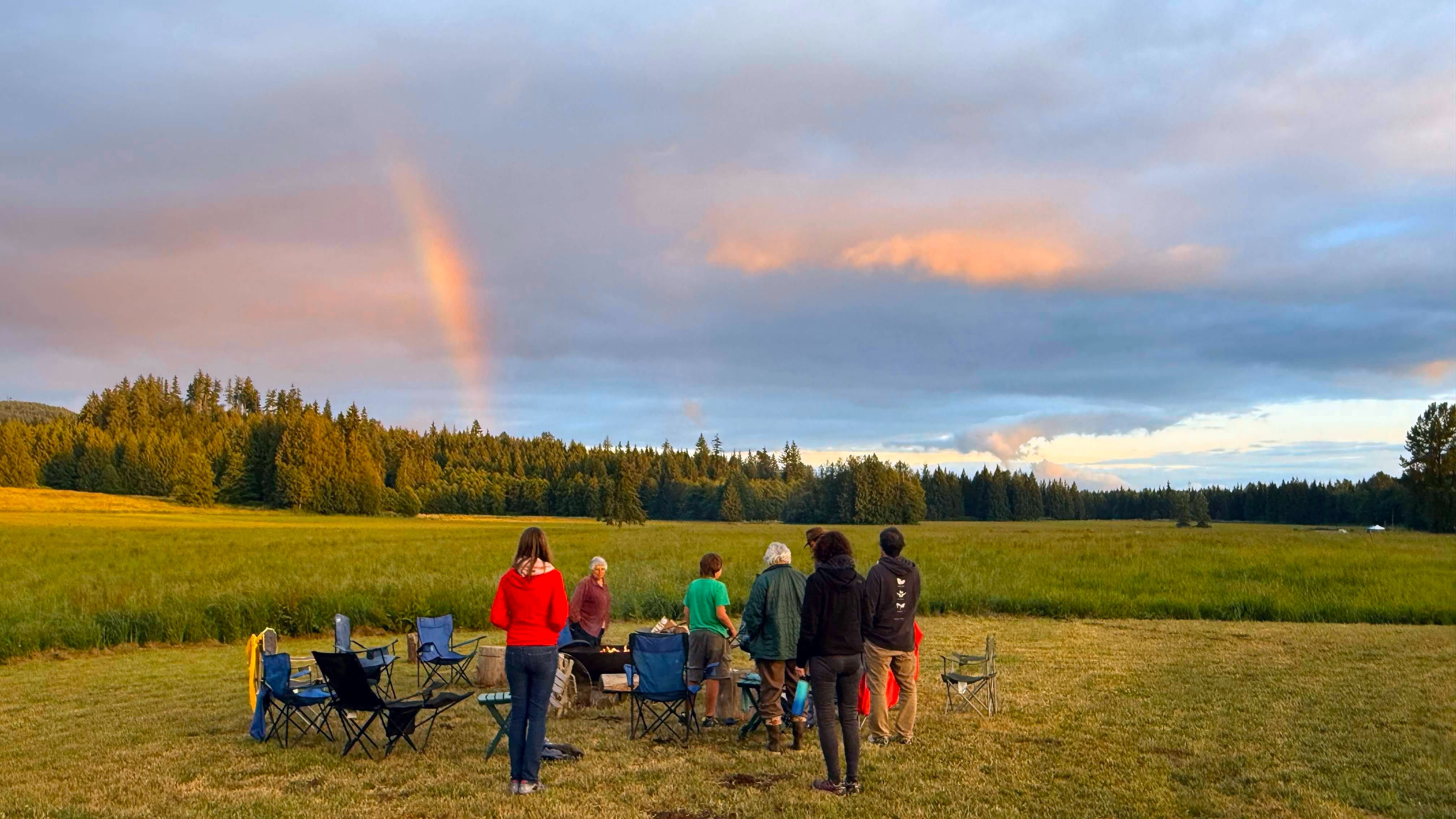 Rooted Northwest community members standing together in a field at dusk with a rainbow over farmland