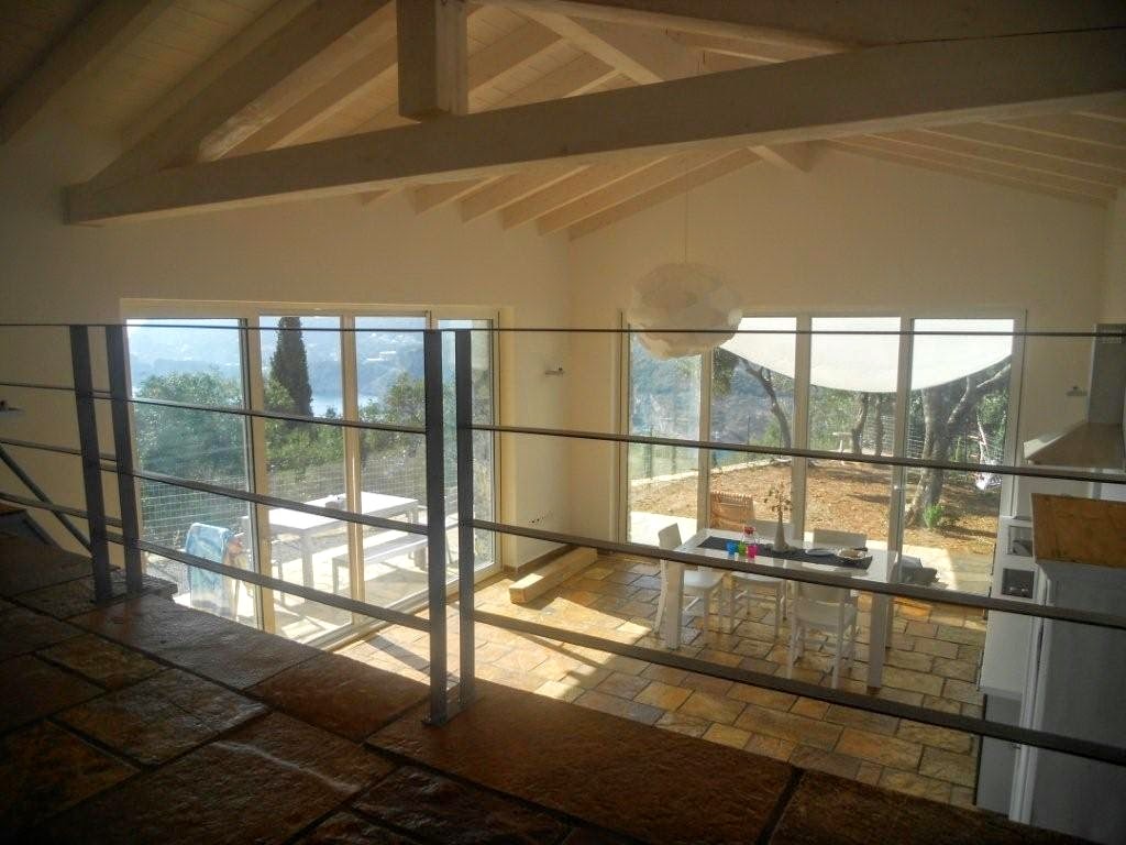 Interior view of Villa Calivi with wooden ceiling beams and large windows overlooking the Ionian Sea.