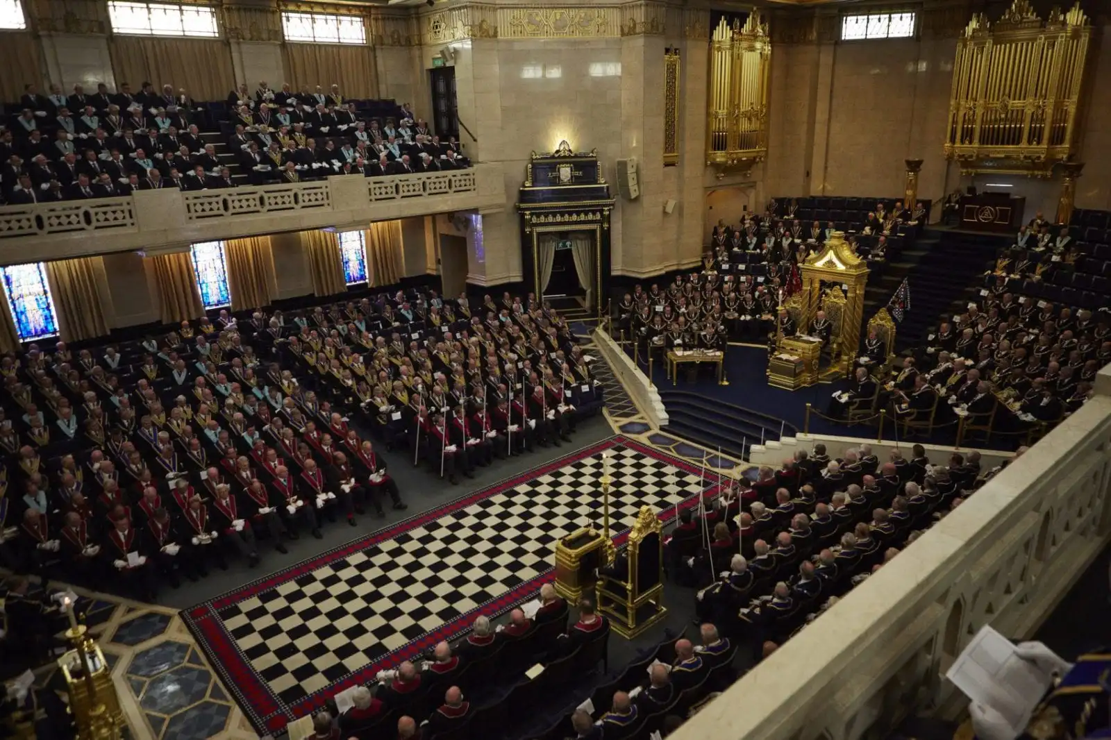 Grand Masonic lodge ceremony with hundreds of Freemasons in regalia gathered in an ornate hall with a black and white checkered floor