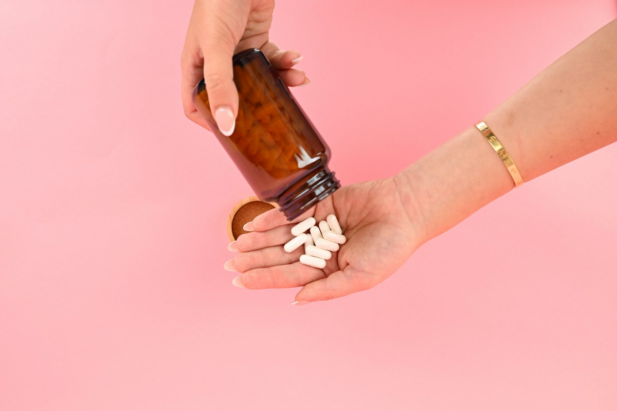 A person pouring white probiotic capsules from a supplement bottle into their hand.