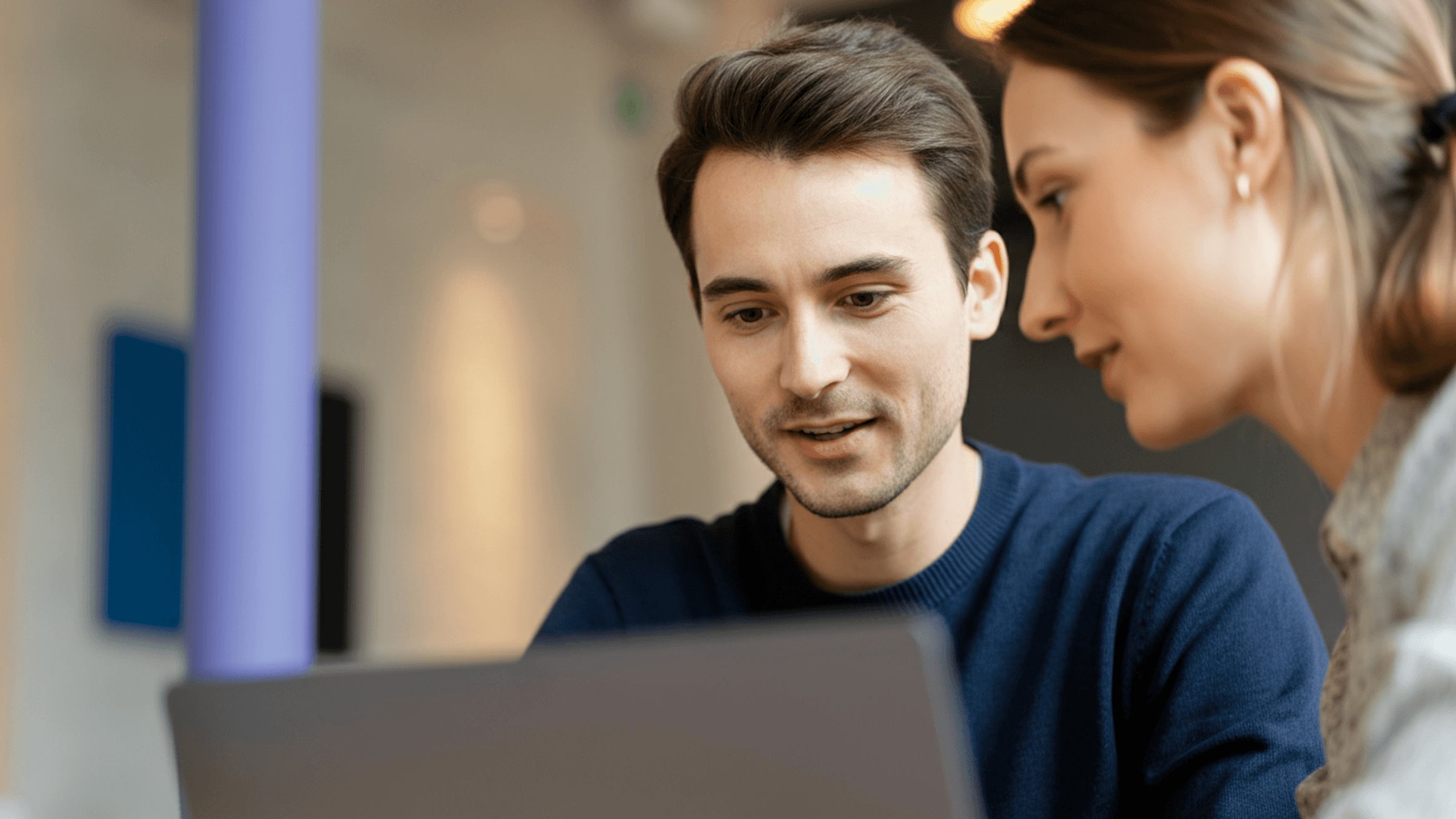 Two colleagues collaborating on a project, focused on a laptop screen in a modern office setting.