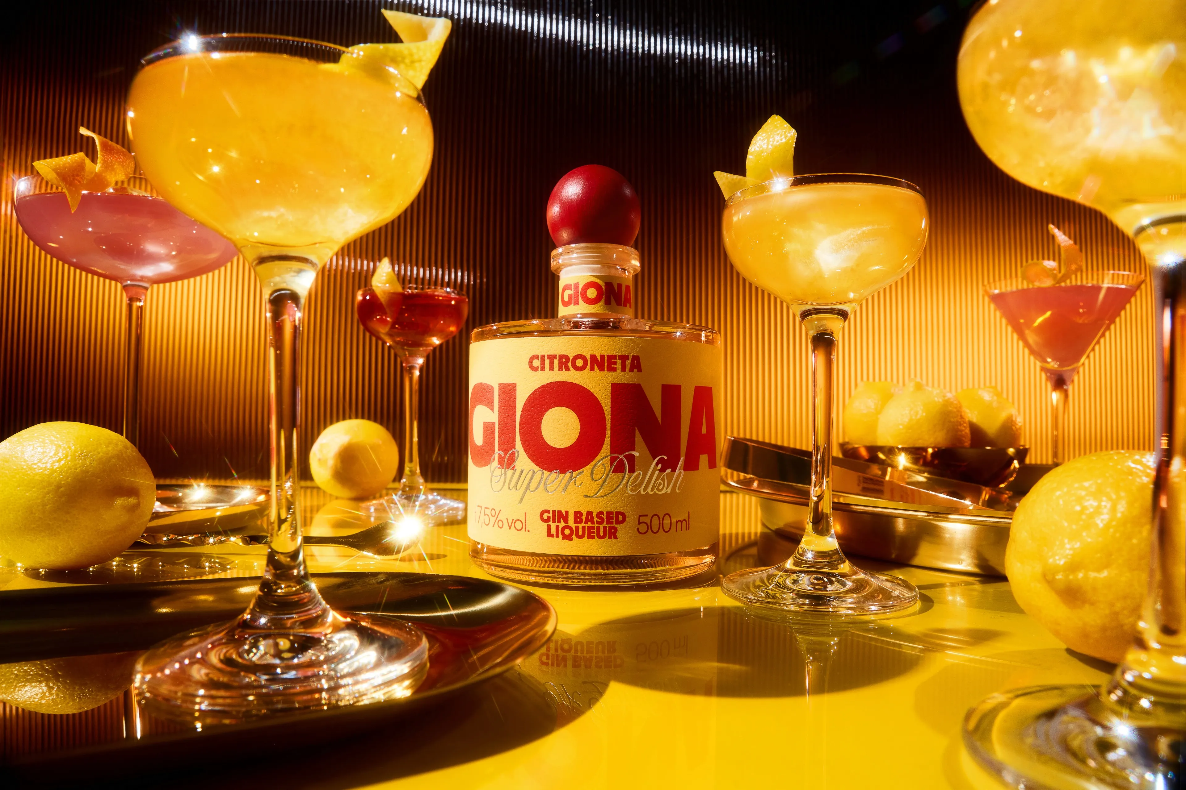 Giona Citroneta bottle surrounded by lemon cocktails in coupe glasses on a yellow surface, liqueur branding
