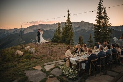Dinner guests watch the couple dance on the overlook beneath string lights at dusk.