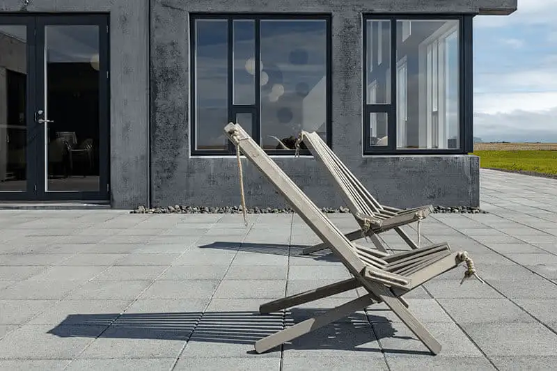Two wooden deck chairs on a stone patio outside the hotel's large windows