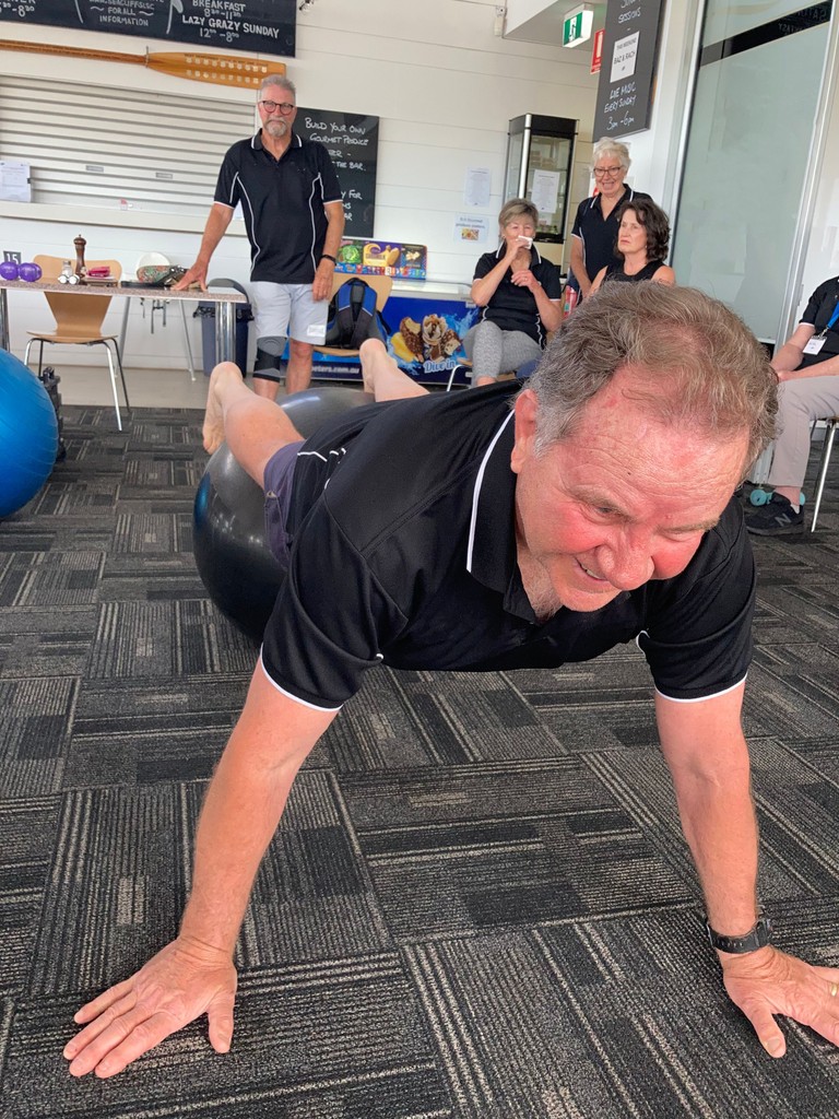 A man holding a plank over a gym ball during a group exercise class.